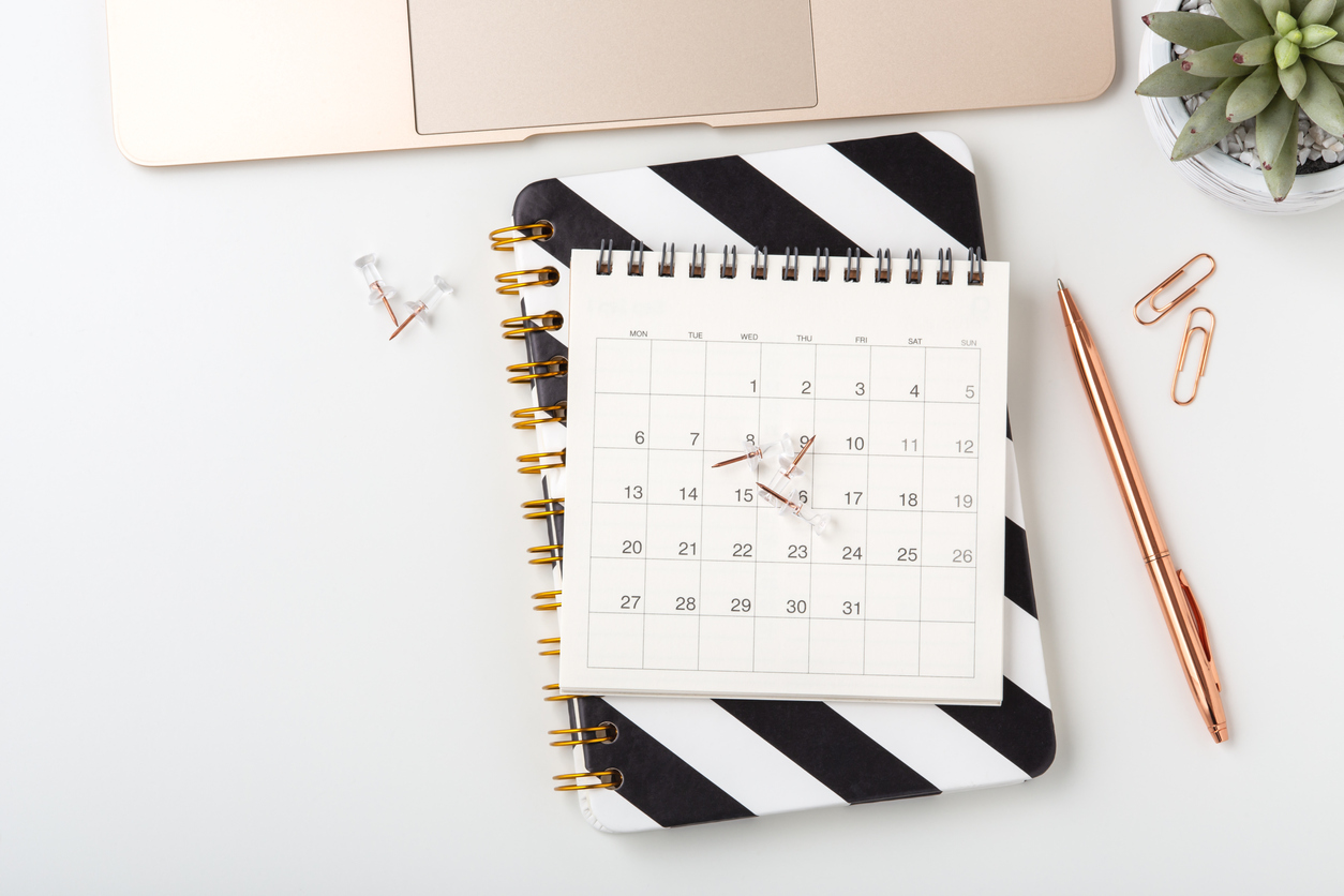 Calendar on notebook with pen and laptop on white desk, flat lay, business meeting, event planning concept