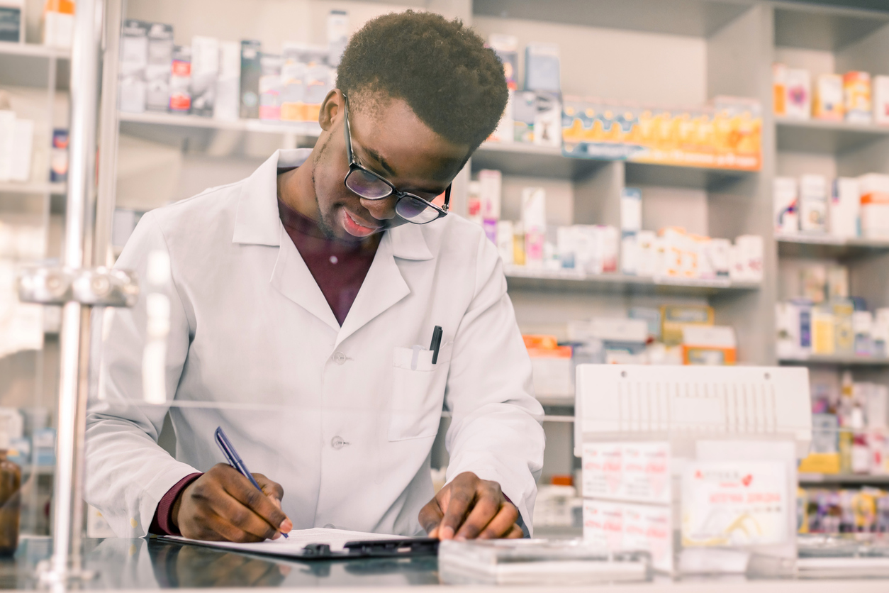 Portrait of a happy African American pharmacist writing prescription at workplace in modern pharmacy.