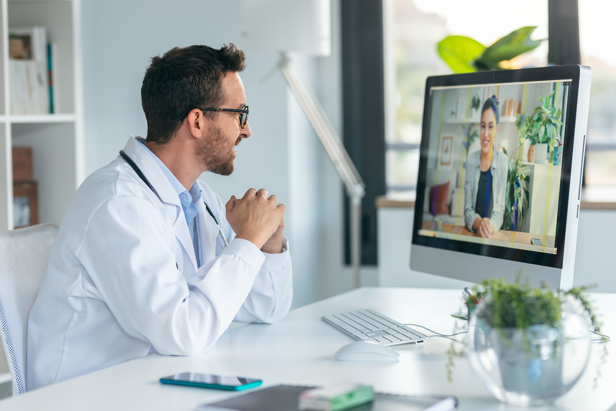 Shot of mature male doctor talking in a video call with computer in the consultation.